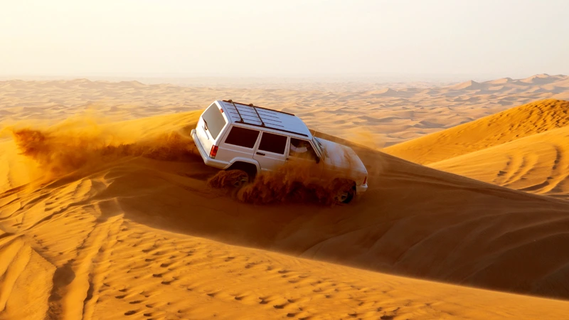 Desert safari in Dubai featuring dune bashing in golden sand dunes with a 4x4 vehicle under a clear sky.
