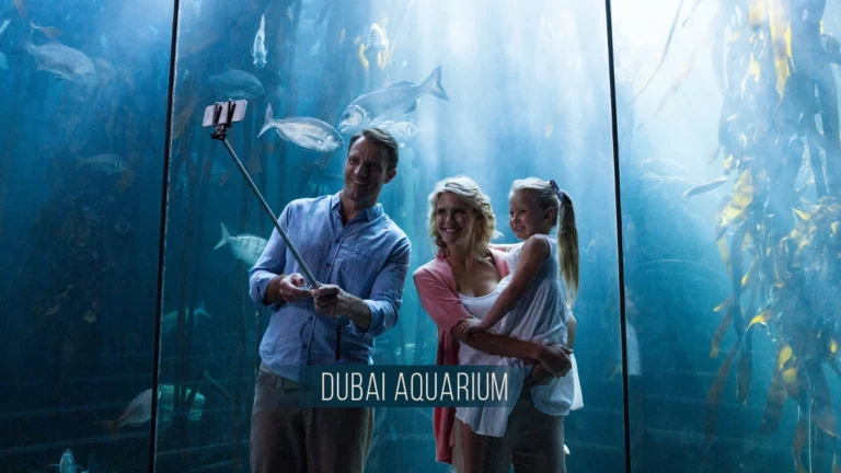 Family taking a selfie inside Dubai Aquarium tunnel surrounded by large fish and marine life.